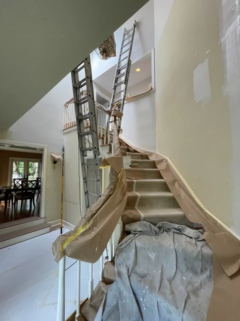 Interior stairwell with protective coverings, ladder, and drywall preparation for painting