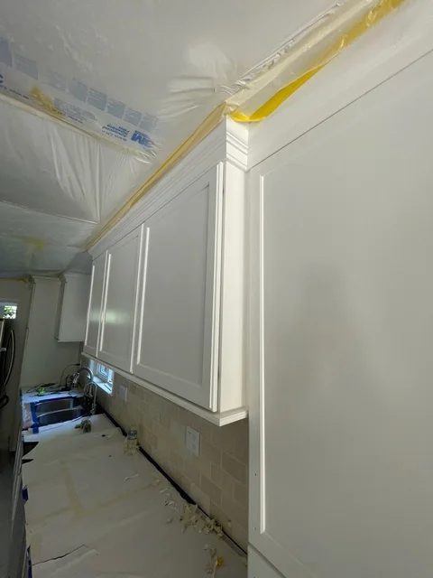 Interior room with freshly painted white walls and cabinets, protective plastic sheeting on ceiling
