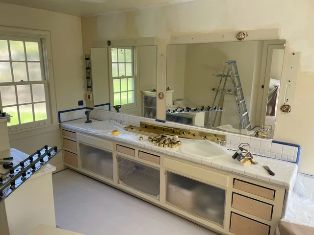 Bathroom vanity with fresh white paint, large mirror, and refinished cabinetry during renovation