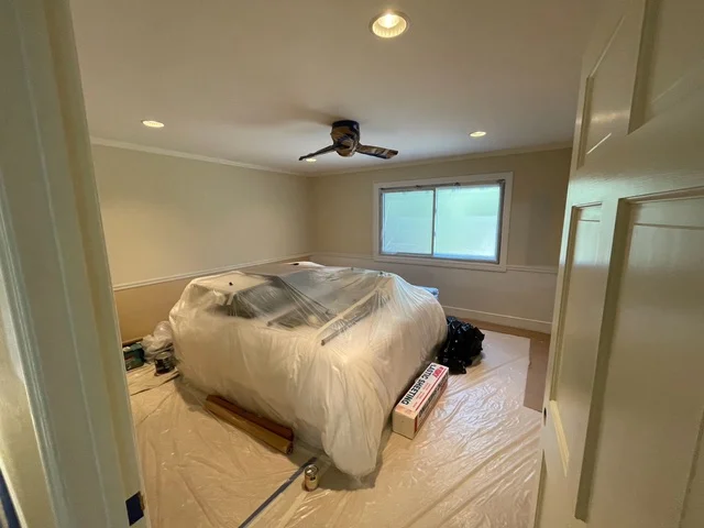 Bedroom interior with freshly painted walls, protected furniture, and new ceiling fan installation