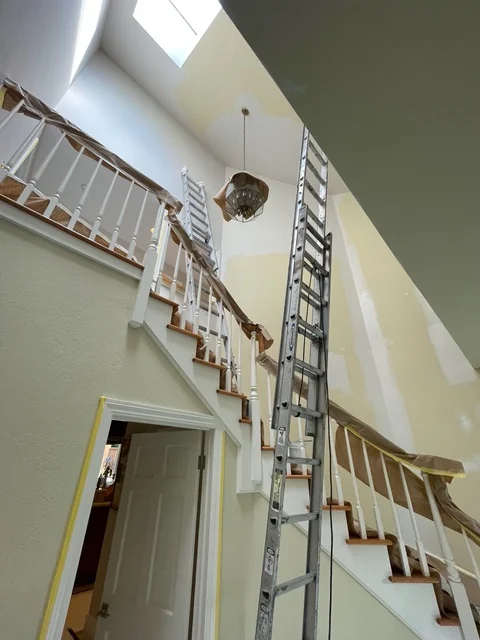 Bright stairwell with white walls, yellow trim, and protective coverings on wooden railings during painting project