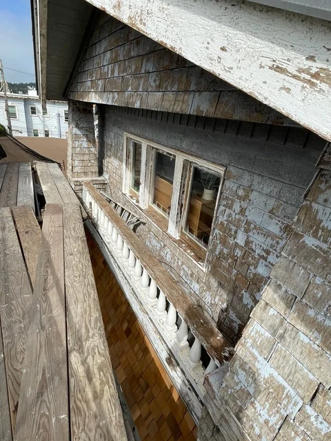 Weathered wood siding with peeling white paint on residential exterior wall and overhang
