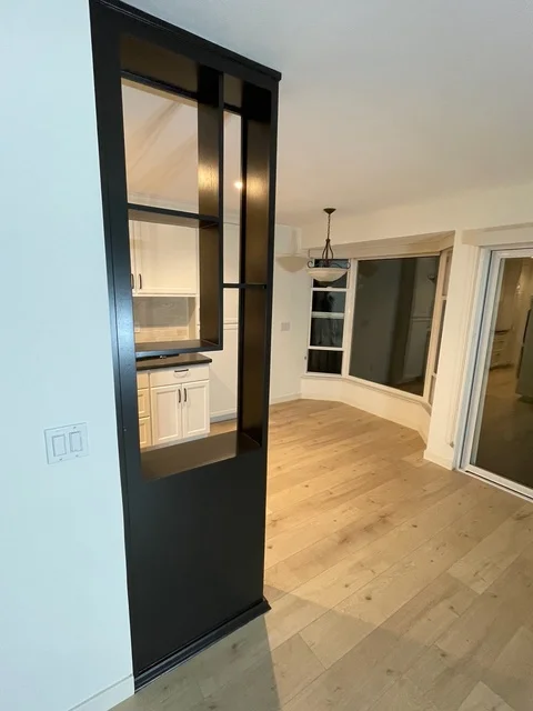 Black framed glass door separating kitchen from living room with white walls and hardwood floors