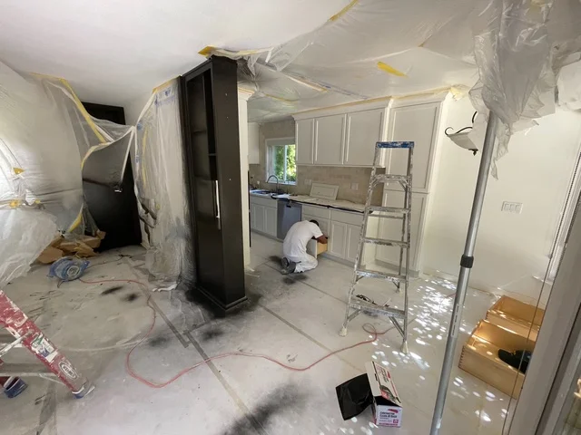 Kitchen interior with protective plastic sheeting, masked support column, and preparation for painting