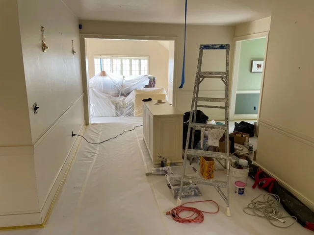 Interior painting project with protective plastic sheeting, drop cloths, ladder, and paint supplies during preparation phase