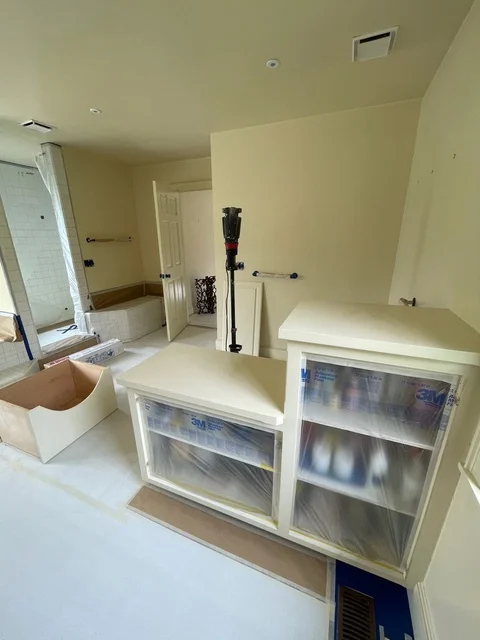 Interior room with primed walls, protected cabinets, and preparation materials for painting project